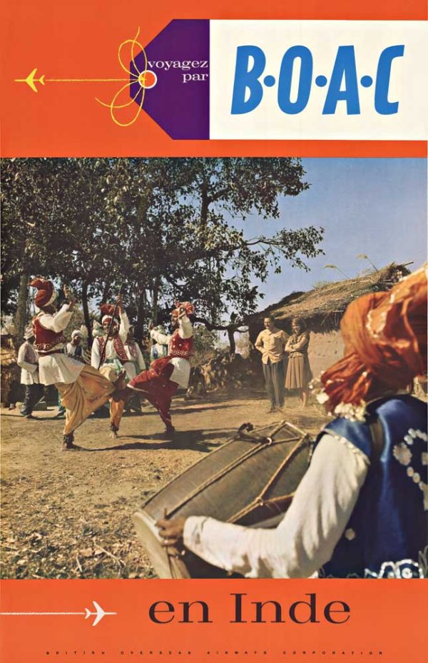 Colorfully dressed dancers perform in a village setting while a seated drummer plays in the foreground, with onlookers and trees behind them.