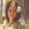 Portrait of a woman with a flower in her hair surrounded by tropical foliage against a soft natural background.